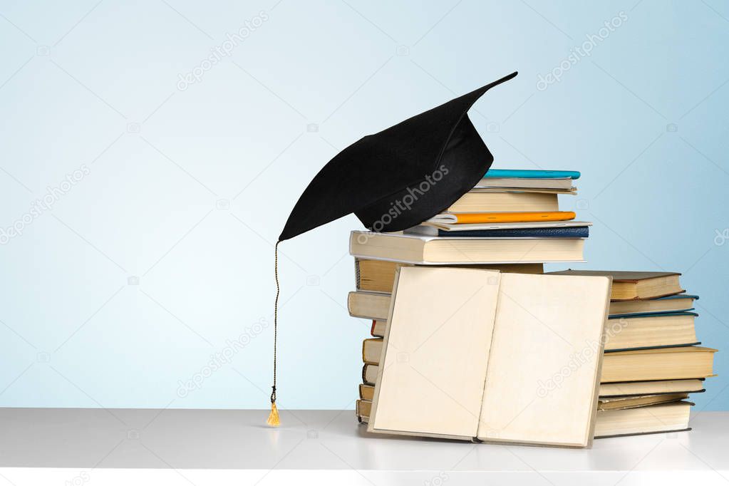 books and mortarboard on wooden table