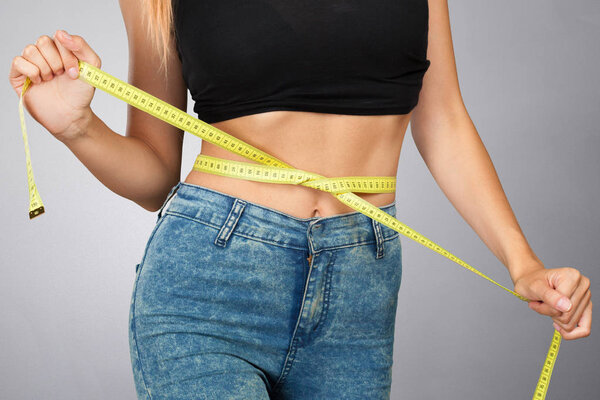 Спортивная стройная женщина измеряет талию с помощью скотча.
 