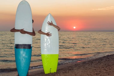 Gün batımında sahilde panoları arkasında ayakta sörfçü genç çift 