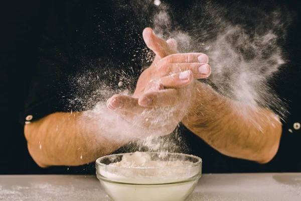 the chef hands are dropping flour over a wooden table