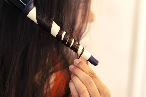 Hairstylist curling hair client in hairdressing salon