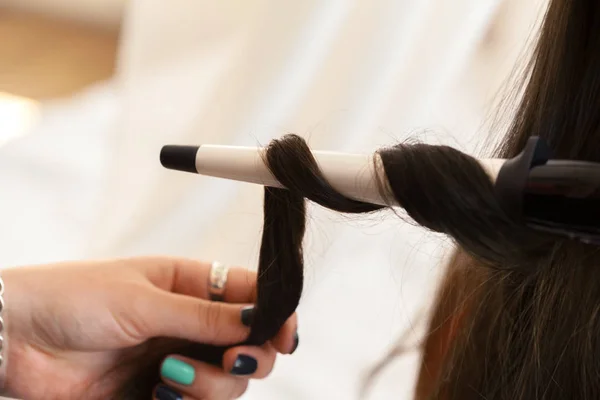 Hairstylist curling hair client in hairdressing salon