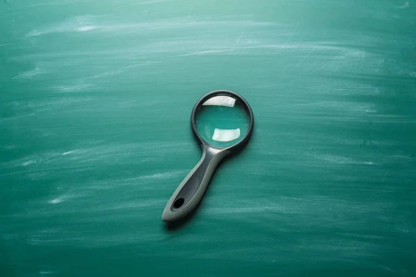 Magnifying Glass on green chalkboard, close-up view