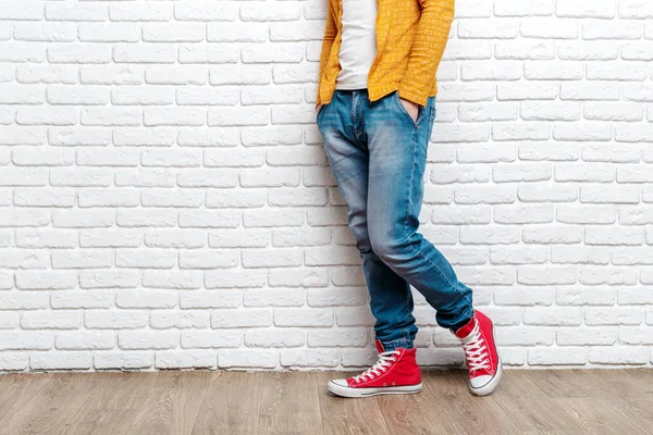 Genç adamın bacakları kot pantolon ve spor ayakkabı ahşap zemin üzerinde moda