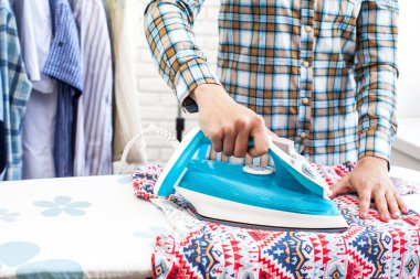 Ütü masasında giysileri ütüleyen bir kadın.