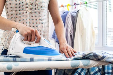 Ütü masasında giysileri ütüleyen bir kadın.