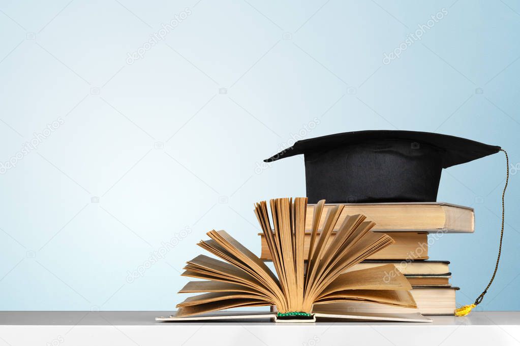 books and mortarboard on wooden table