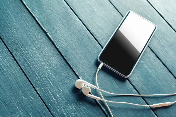 white earphones attached to smartphone on wooden background