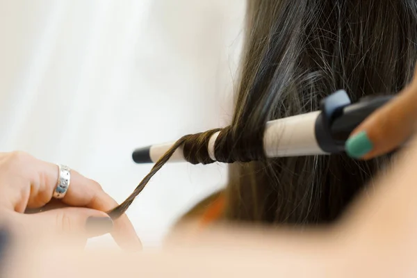 Hairstylist curling hair client in hairdressing salon