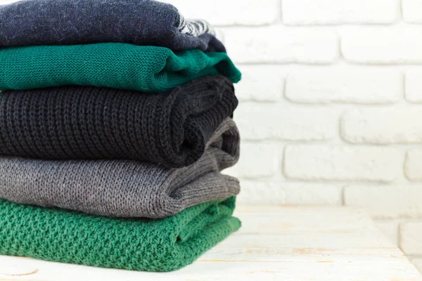 Stack of white cozy knitted sweaters on wooden table , close-up