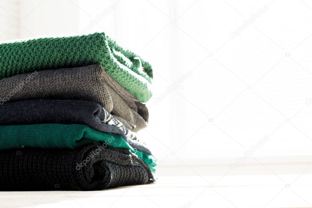 Stack of white cozy knitted sweaters on wooden table , close-up 