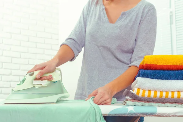 Ütü masasında giysileri ütüleyen bir kadın.