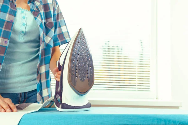 Ütü masasında giysileri ütüleyen bir kadın.