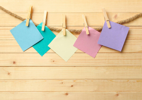 clothespins hanging with blanks paper on wooden background