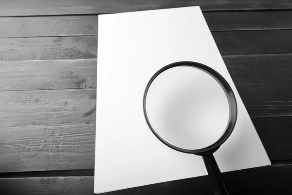 Magnifying glass and blank paper on wooden table