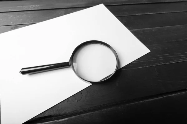 Magnifying glass and blank paper on wooden table