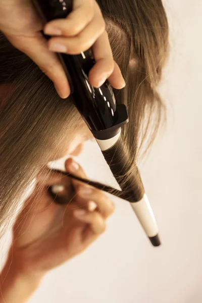 Close view of hair stylist curling hair client in hairdressing salon