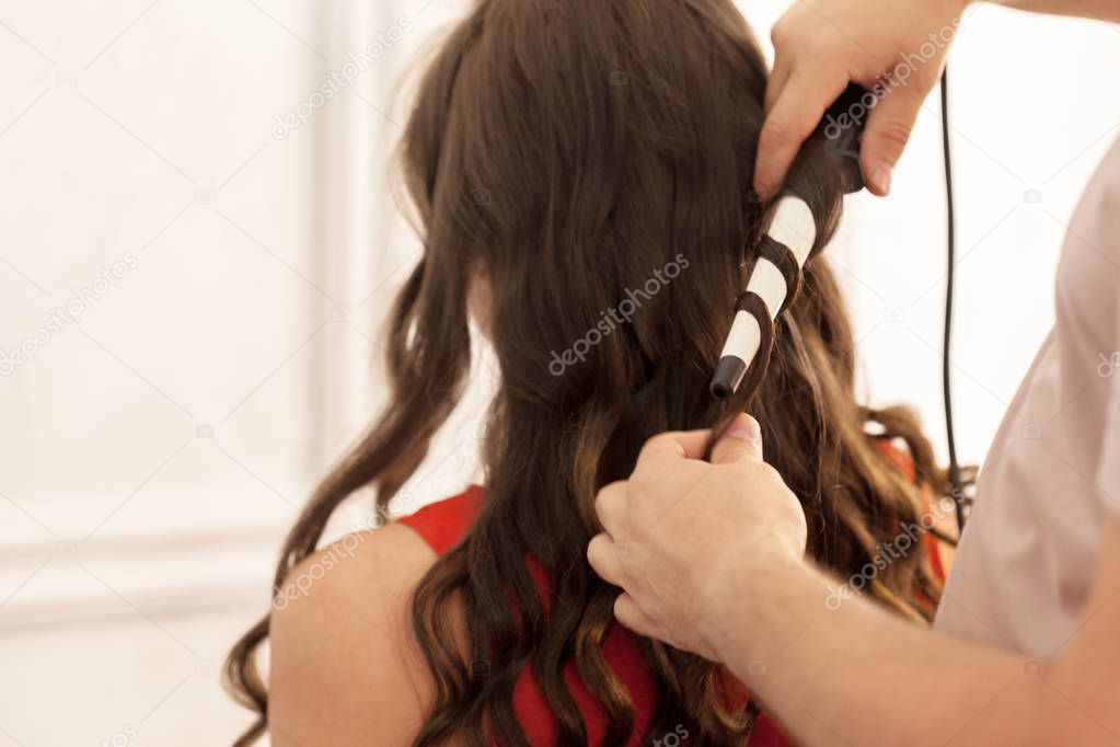 Close view of hair stylist curling hair client in hairdressing salon