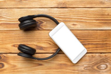 ahşap masa üzerinde akıllı telefon ve kulaklık üstten görünüm