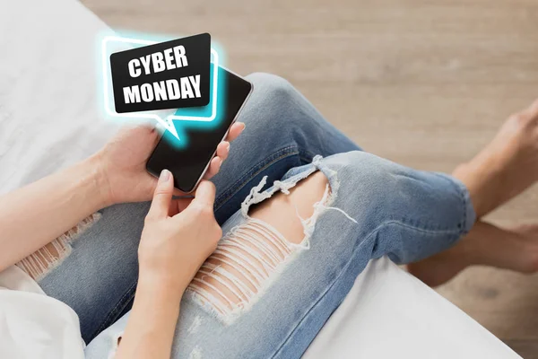 cropped shot of woman checking smartphone with cyber monday inscription on couch