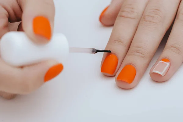 cropped image of woman painting nails in orange