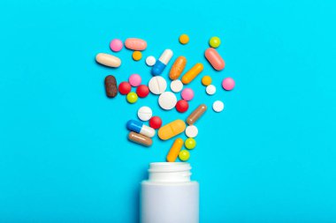 renkli hapları şişeden mavi arka plan üzerinde dağınık.