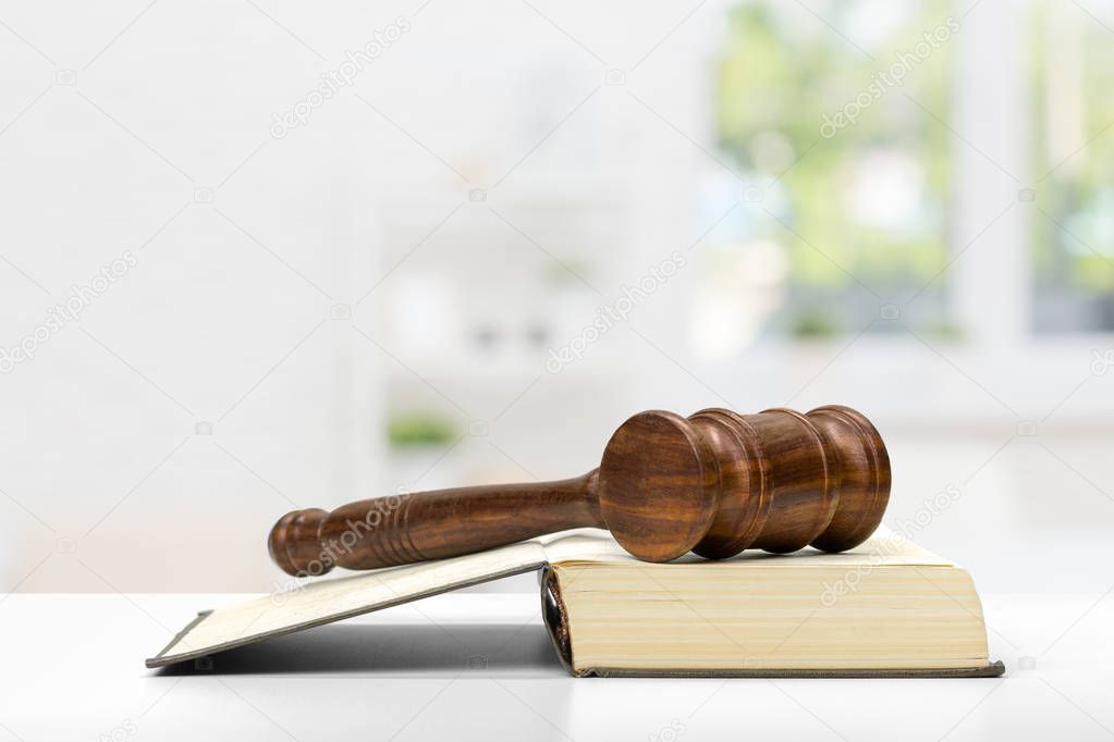 Wooden judge gavel on open book on white table