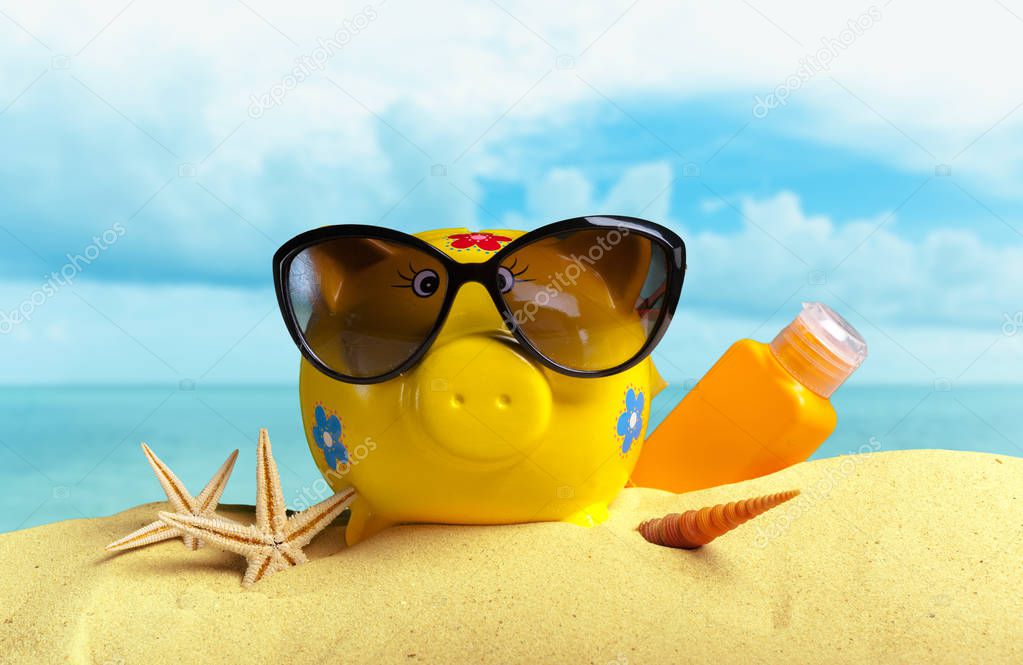 Summer piggy bank with sunglasses on the beach