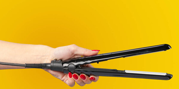 Woman hand with a hair iron isolated on a color background