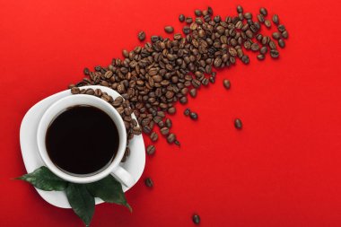 Kahve fincanı kırmızı zemin üzerine kahve çekirdekleri ile.