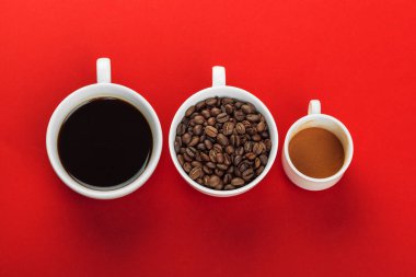 Kahve fincanı kırmızı zemin üzerine kahve çekirdekleri ile.