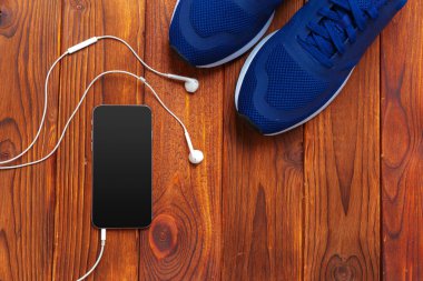 Spor ayakkabı, ahşap masa üzerinde kulaklık ile cep telefonu