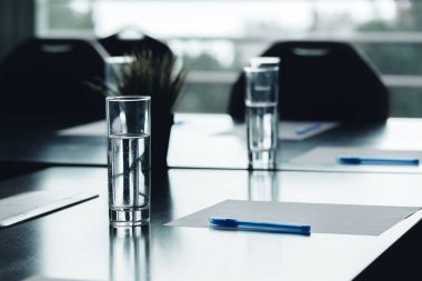 Karanlık konferans masa su bardağı kalem, kağıt sayfalarının yakın çekim