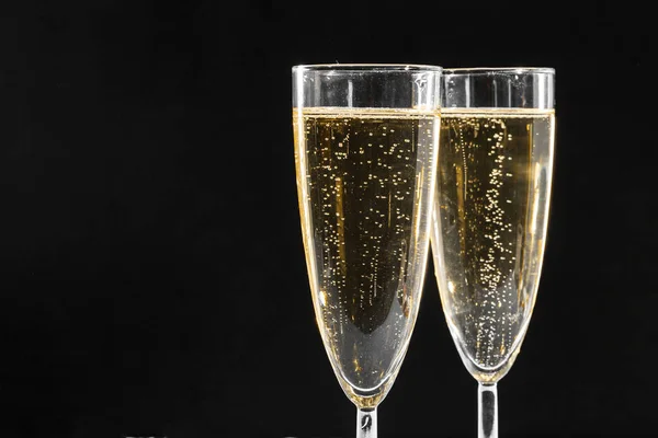 close up of two glasses of sparkling wine against blakc background