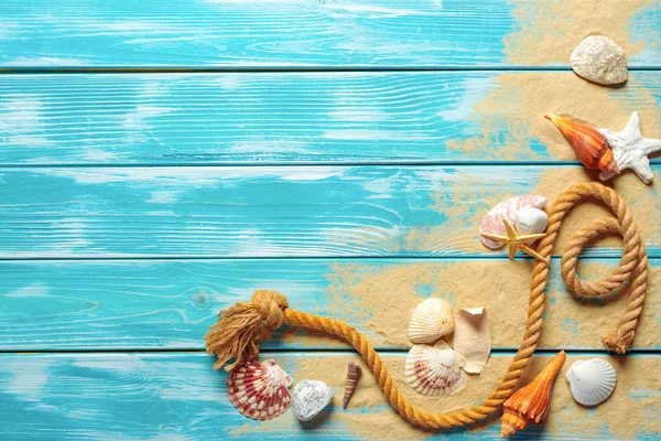 sea rope with sea shells on sea sand on blue wooden background. Top view