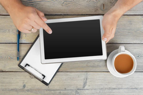 hands of a man holding blank tablet device over a wooden workspace table