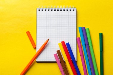 Parlak sarı arka plan üzerinde keçeli kalemler ve boş not defteri