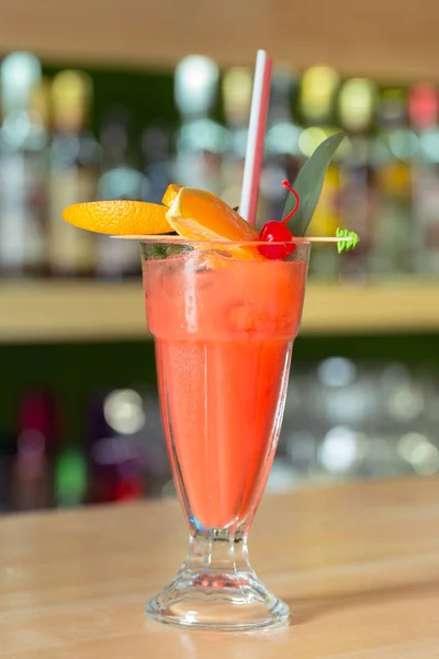 Glass of cocktail decorated with fruits at bar counter background.