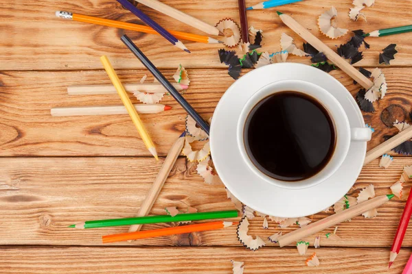 Coffee cup with pencils and pencil cuts on wooden background