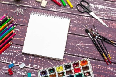 Çizim aletleri, sabit malzemeler, sanatçının çalışma yeri. Suluboya resimler ve ahşap masadaki boş not defteri.