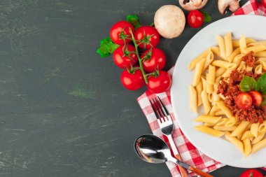 Etli makarna, domates sosu ve sebzeler masada.