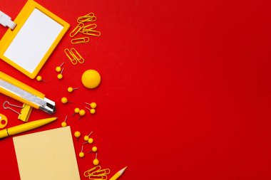 Üst kattaki ofis masasında yatıyordu. Çalışma alanı boş yapışkan notlar, kırmızı arkaplanda ofis malzemeleri.