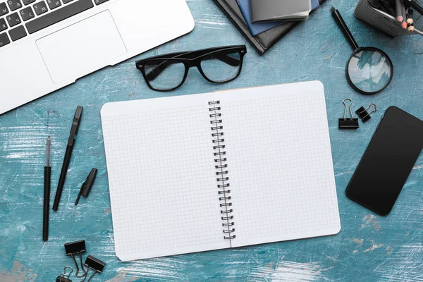 Opened notebook and other office equipment such as computer, pencil,  and glasses on wooden office desk.