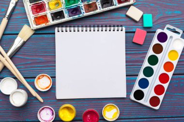 Çizim aletleri, sabit malzemeler, sanatçının çalışma yeri. Suluboya resimler ve ahşap masadaki boş not defteri.