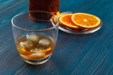 Koyu ahşap arka planda portakal meyveli viski bardağı.