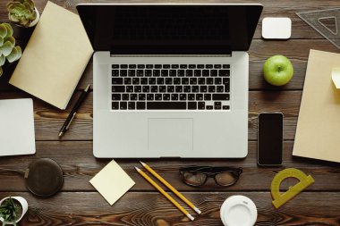 Dizüstü bilgisayar, sarf malzemeleri ve yeşil elma ile Ofis masası, üst görünüm