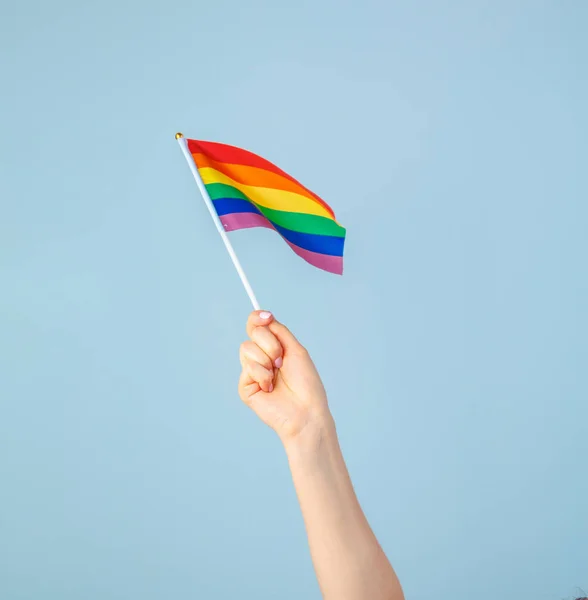 水色の背景に小さな虹の旗を振る手のクローズアップ — ストック写真