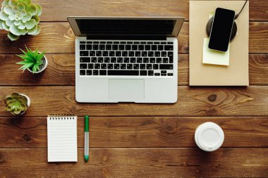 Ofis masası çalışma alanı üst görünümü. Dizüstü bilgisayar, cihazlar ve tesis içeren ahşap masa