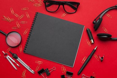 Üst kattaki ofis masasında yatıyordu. Boş not defteri olan çalışma alanı, kırmızı arkaplanda ofis malzemeleri.