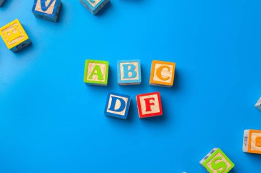 Abcdf' e. Mavi arka plan üzerinde ahşap renkli alfabe blokları, düz yatıyordu, üst görünüm. 